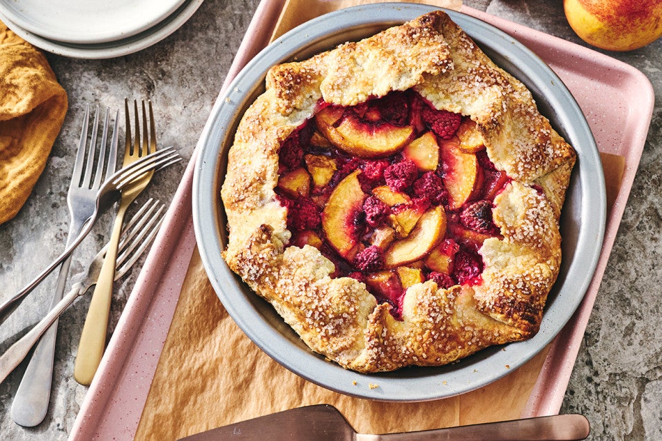 Photograph of Rustic Raspberry-Peach Pie from above with a perfectly browned folded crust around the edges of a vibrant raspberry and peach filling.