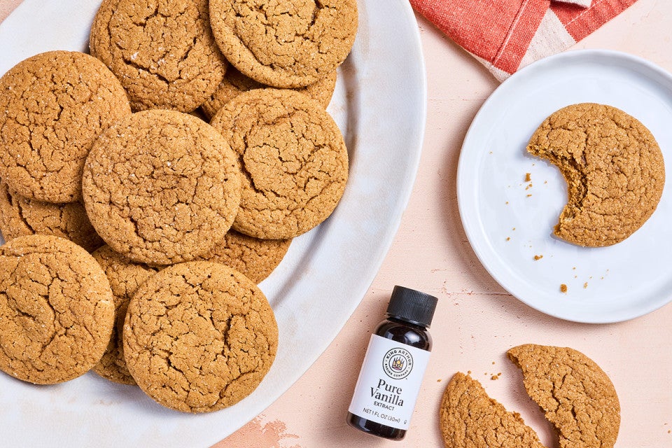 Soft Brown Sugar Cookies spread out on various plates with a small jar of King Arthur Baking Vanilla Extract.