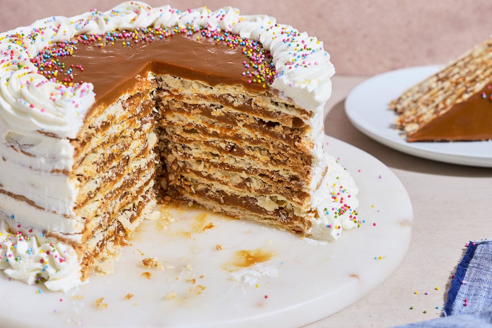 Torta Chilena photographed from the side showing a generous slice removed with layers of dulce de leche, crispy pastry, and creme fraiche frosting.