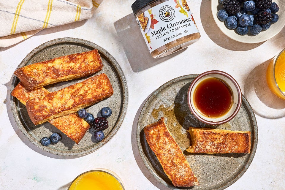 French Toast Sticks on plates with a small dish of maple syrup, King Arthur Baking Maple Cinnamon french toast sugar, and berries.