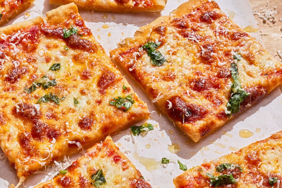 Slices of Gluten-Free Sheet Pan Pizza showing a classic cheesy pizza with brown bubbly cheese and drops of basil pizza topping.