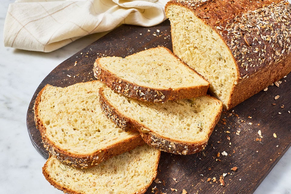 Multigrain Protein Bread partially sliced on a dark brown cutting board.