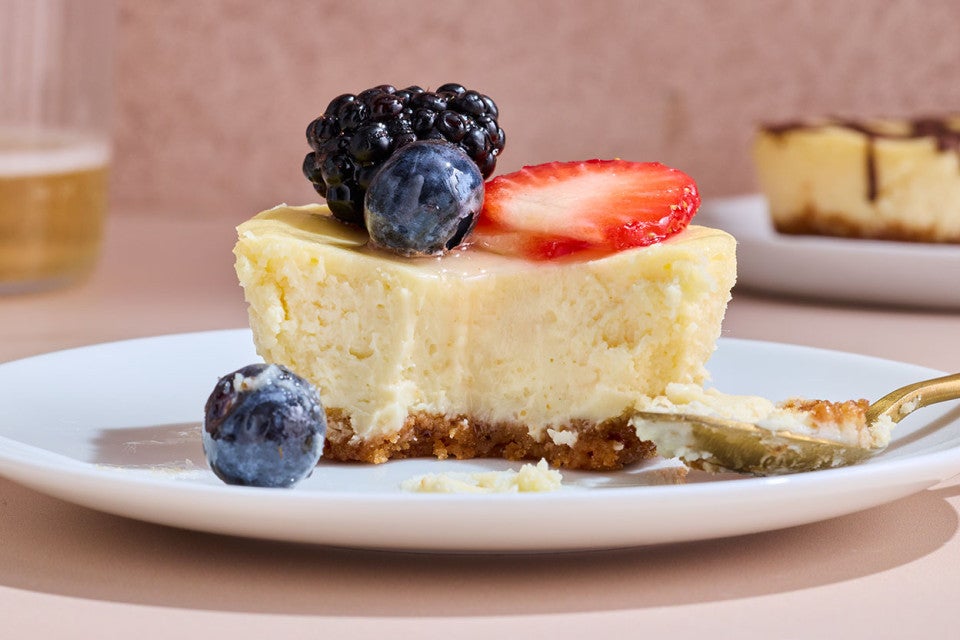 A Mini Cheesecake on a plate seen from the side showing a smooth interior and short-crust on the bottom with fresh berries on top.
