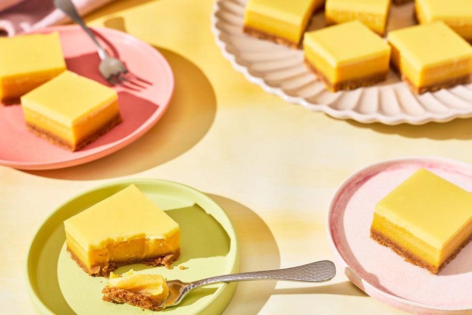A table set with pastel colored tableware and plates with Passionfruit Bars spread out.