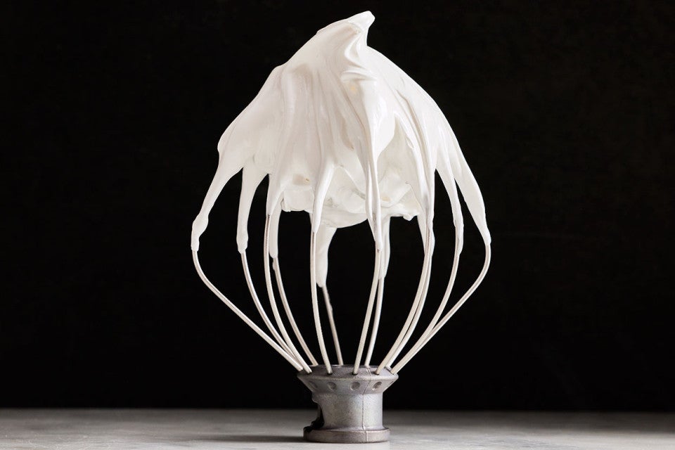 White Swiss Meringue on a mixer whisk shown upright against a black background.
