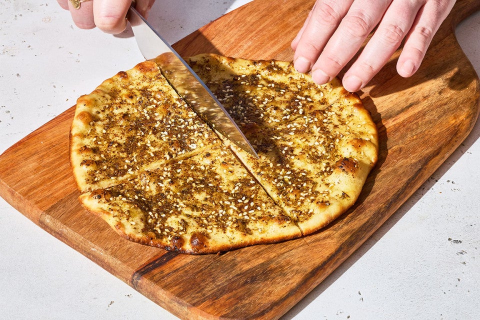 Slicing Za’atar Manakeesh ona. wooden cutting board.