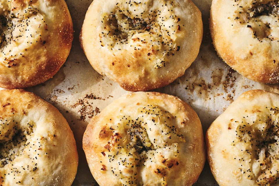 Classic Bialys on a sheet tray fresh out of the oven showing a beautiful crust and herbs on top of them.