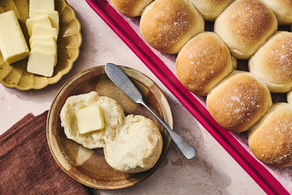 Big-Batch Quick Dinner Rolls on a sheet tray and one a plate with butter.