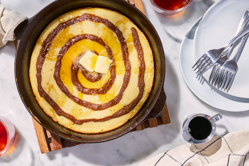 A Cinnamon Roll Skillet Pancake in a skillet shown on a table with plates and forks next to it.