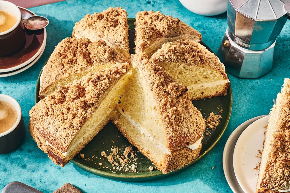 A round, Cream-Filled Coffee Cake, sliced on a dark plate with other breakfast elements spread around a table.