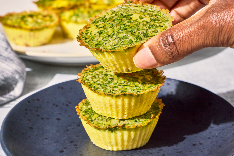 Egg Bites stacked on a plate with a hand picking one up off the top.