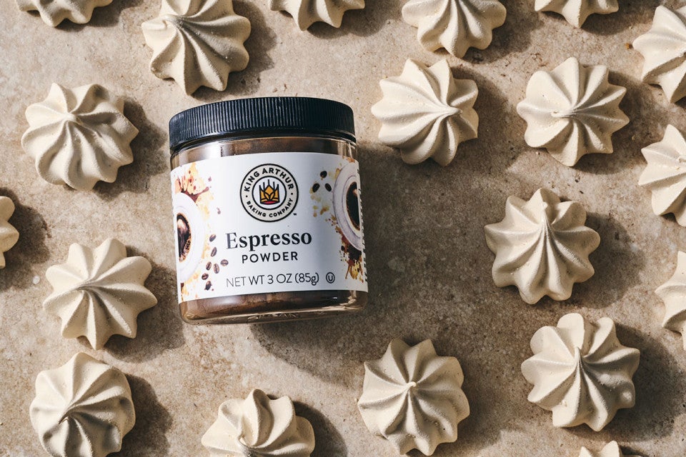 Espresso Meringue powder from King Arthur Baking in laid on its side among many meringues spread on a neutral textured counter.