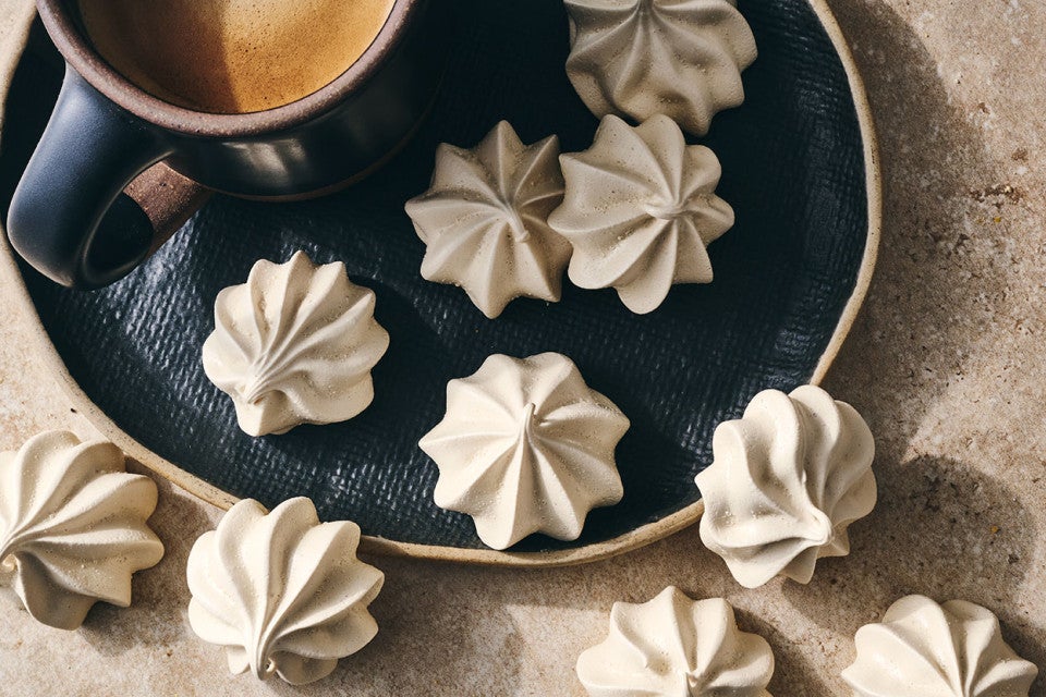 Espresso Meringues photographed from above and randomly spread on a dark plate with a cup of coffee in the upper left of the image.