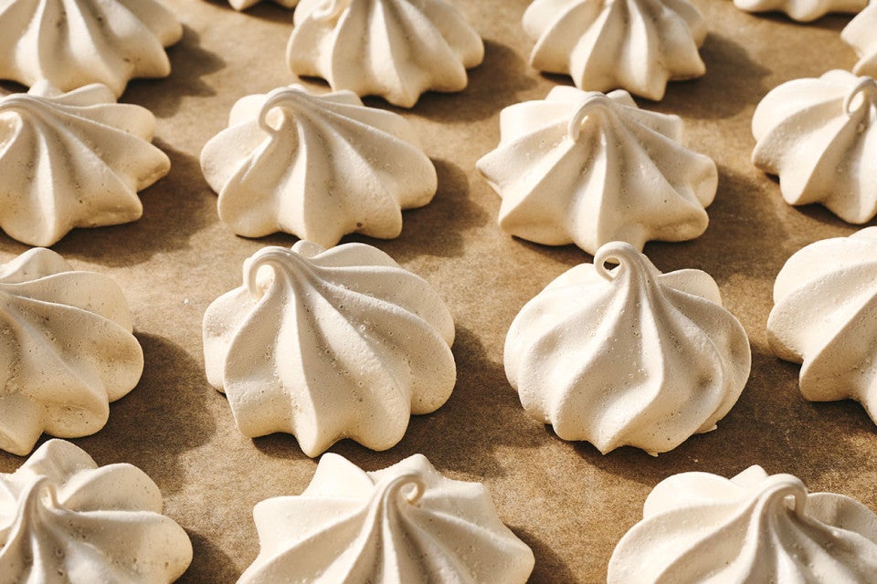 Several Espresso Meringues shown piped and baked on a neutral background with a swirling texture and curled tops.