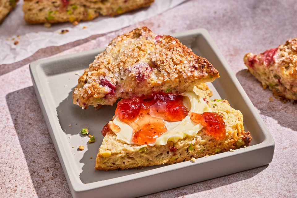 A Roasted Strawberry and Pistachio Scone sliced in half with cream and dollops of strawberry preserve.