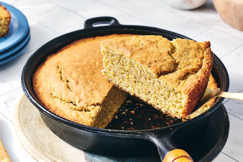 A slice of Sourdough Cornbread being removed from a cast iron skillet.