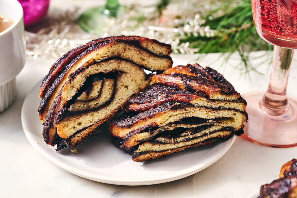 Two slices of chocolate babka wreath on a plate with festive ornamentation around the setting.