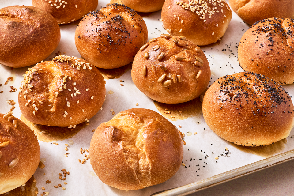 Freshly baked gluten-free rolls on a sheet tray with split tops and a deep golden crust.