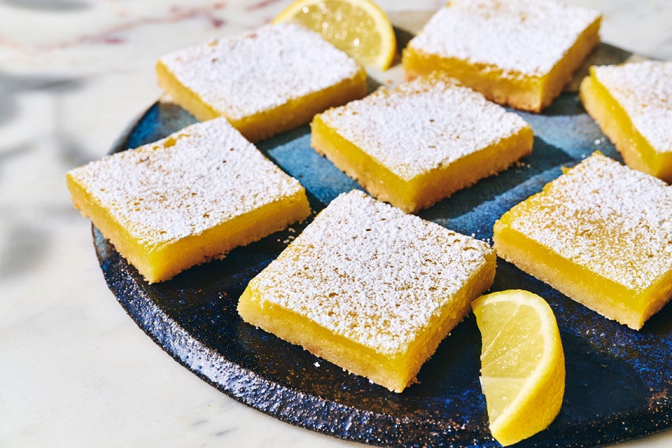 Gluten-Free Lemon Squares with an Almond Flour Crust on a dark plate with a slice of lemon as garnish.