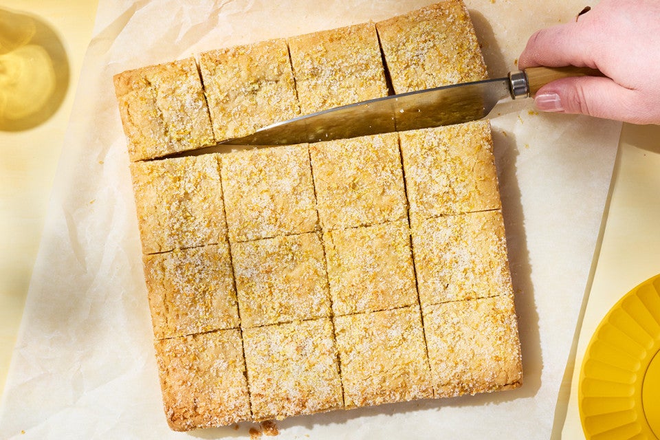 Slicing Alex Roberts Lemon Citrus Blondies on parchment paper atop a counter.