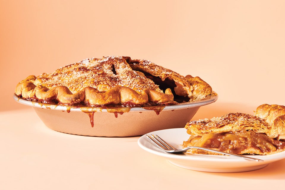 An apple pie in a pie tin and a slice on a plate.