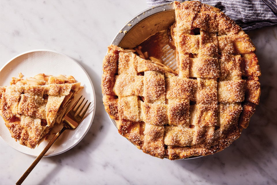 An apple pie in a pie tin and a slice on a plate.
