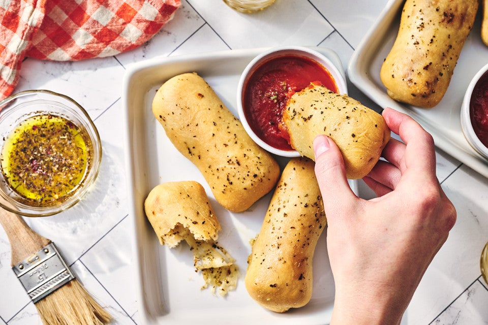 Dipping a Cheese Stuffed Breadstick into a ramekin of tomato sauce.