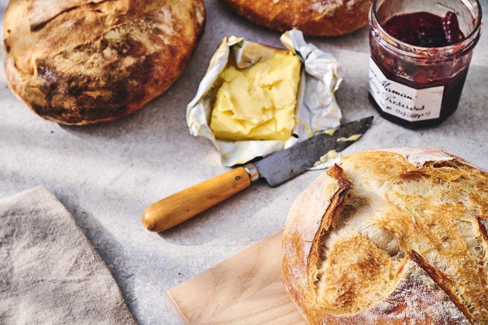 Fresh baked loaves of No-Knead Crusty White Bread on a table with jam and butter
