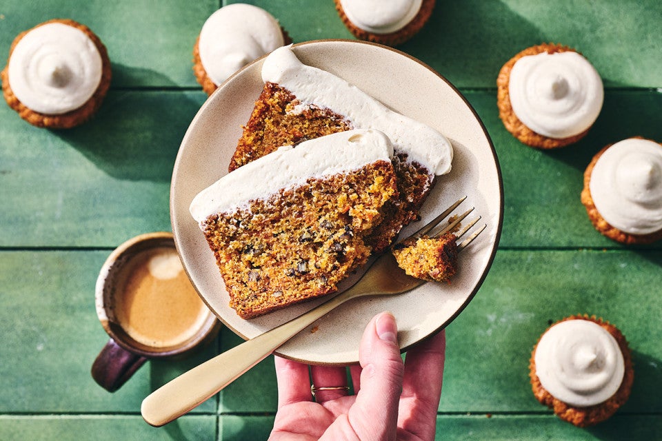 Spiced Carrot Snacking Cake on a plate with a fork and cupcakes in the background.