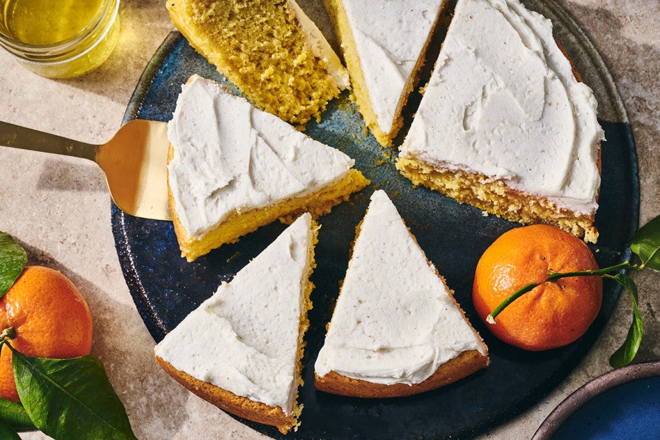 Sliced whole orange cake on a plate with white frosting and an orange.
