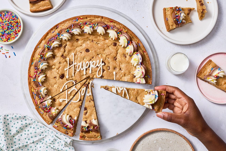 Removing a slice of chocolate chip cookie cake seen from above.