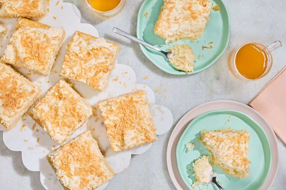 Creamy Coconut Sheet Cake arranged on a counter sliced on a platter, and additional slices on blue green plates