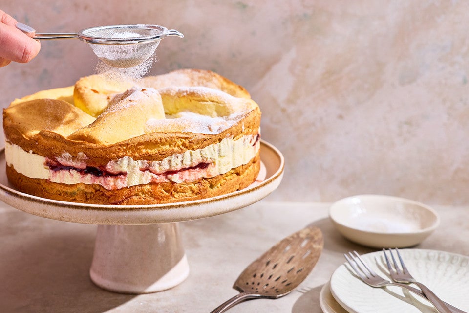 Karpatka Cake on a cake stand being dusted with powdered sugar.