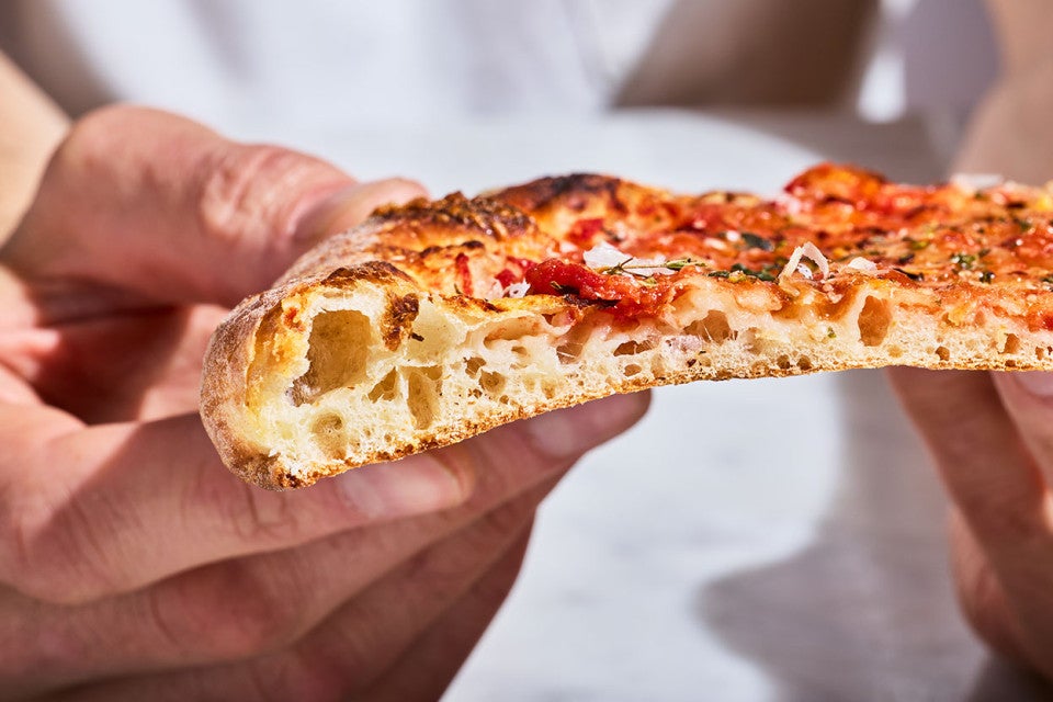 A slice of New York-Style Pizza showing the thin and airy dough from the side.