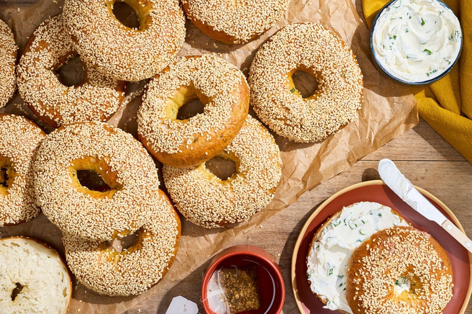 Sesame Sourdough Discard Bagels arranged on parchment with a shmear of cream cheese and a sliced bagel on a plate.