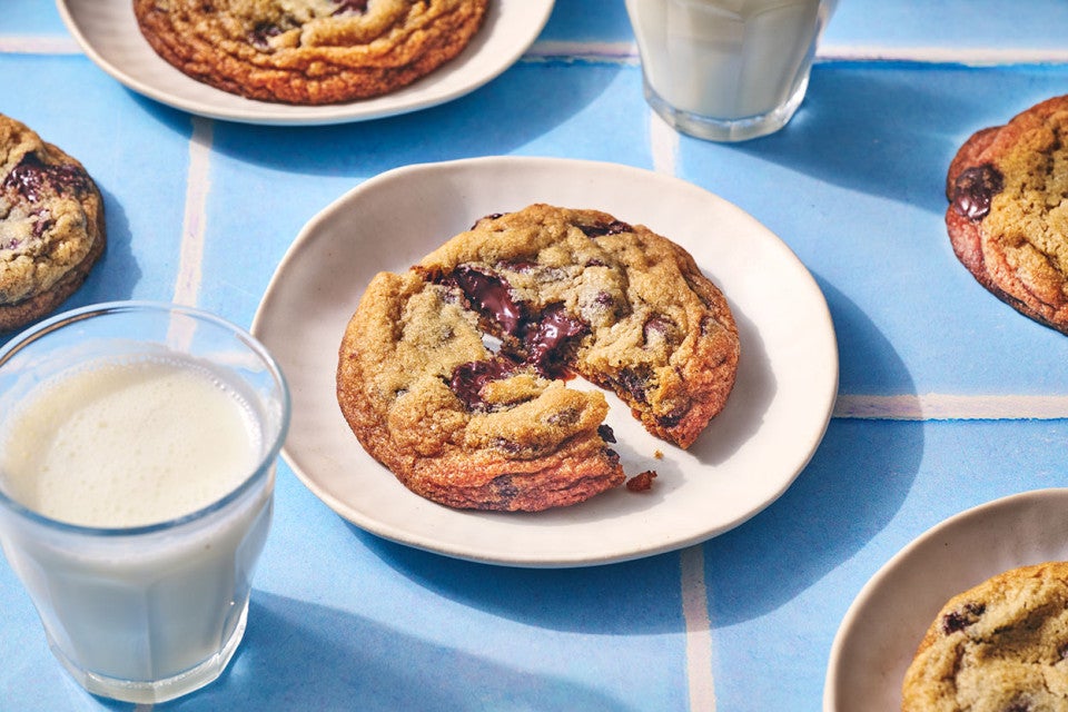 A Classic Chocolate Chip Cookie split on a plate atop a blue counter with glasses of milk in the photo.
