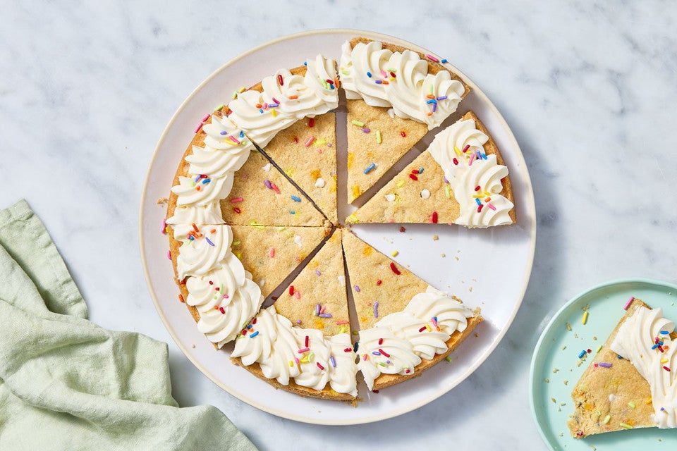 Sliced Confetti Sugar Cookie Cake on a marble countertop with a piece on a plate.
