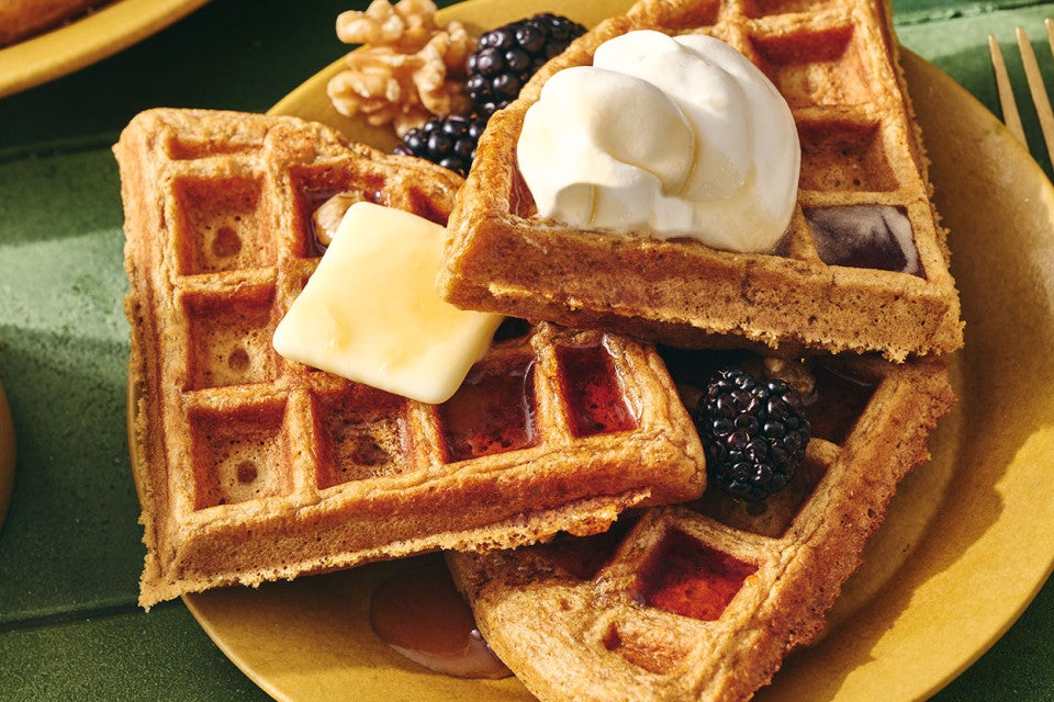 Gingerbread Waffles on a plate with whipped cream, butter, syrup, and fresh berries.