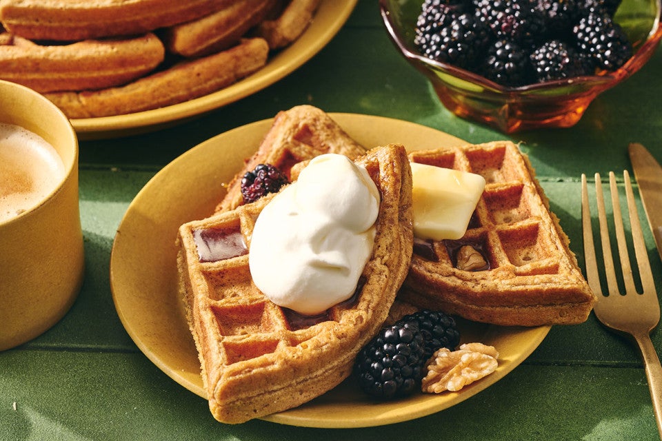 Gingerbread Waffles on a plate with whipped cream, butter, syrup, and fresh berries.