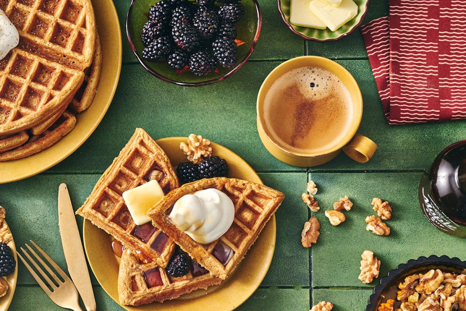 Gingerbread Waffles on a plate with whipped cream, butter, syrup, and fresh berries.