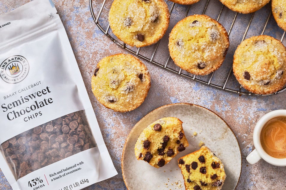 Easy Chocolate Chip Muffins on a plate and a cooling rack with a bag of Semisweet Chocolate chips from King Arthur Baking