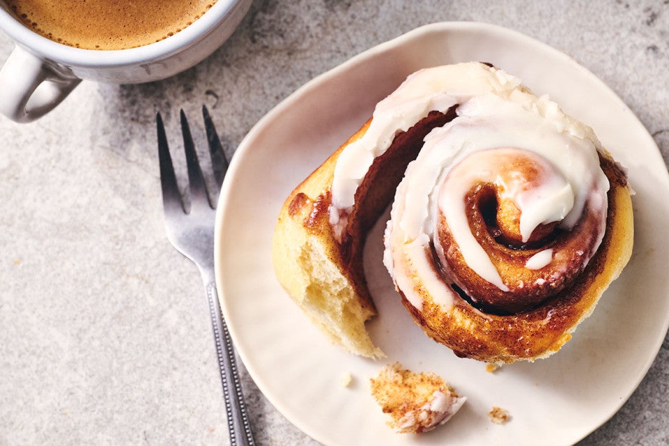 A Sourdough Cinnamon Roll on a plate accompanied by coffee - seen from above.