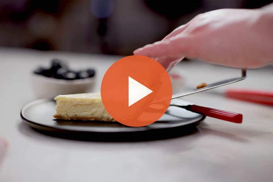 Putting a slice of easy cheesecake on a plate with an orange play icon over the image