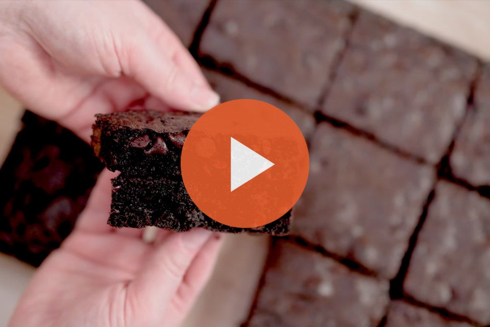 Breaking apart a fudge brownie with an orange play icon over the image.