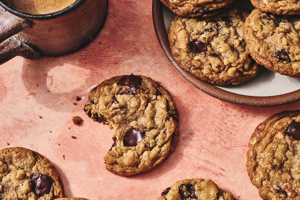 Whole Wheat Oatmeal Cookies on a plate with a mug of coffee and a cookie with a bite taken out on a counter seen from above