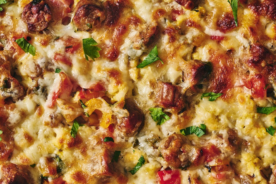Detailed shot of breakfast pizza showing veggies, melted cheese, eggs, sausage, and herbs