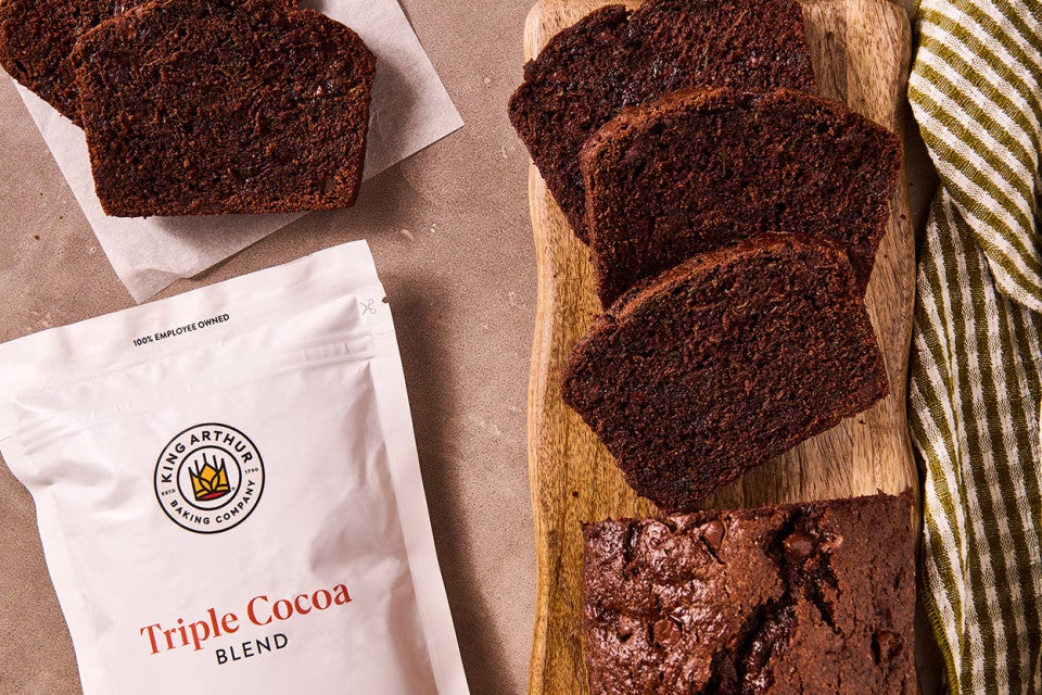 Double Chocolate Zucchini Bread on a cutting board with a bag of triple cocoa blend by King Arthur Baking