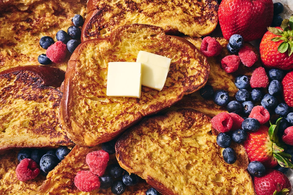 French Toast stacked together with pats of butter and surrounded by fresh berries