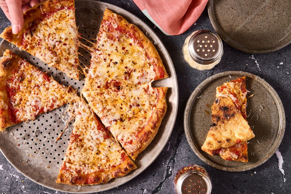 A Gluten Free NY Style Pizza on a pizza pan seen from above.
