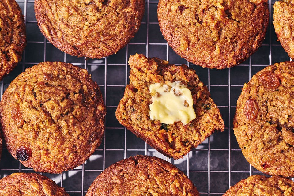 Morning Glory Muffins on a cooling rack. One is split with butter on it.